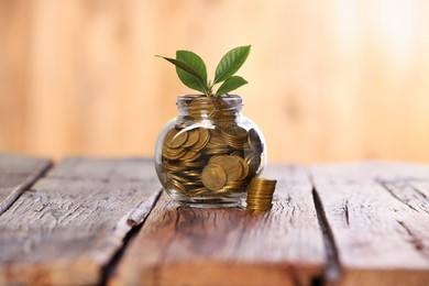 Photo of Investment concept. Glass jar with coins and sprout on wooden table against blurred orange background