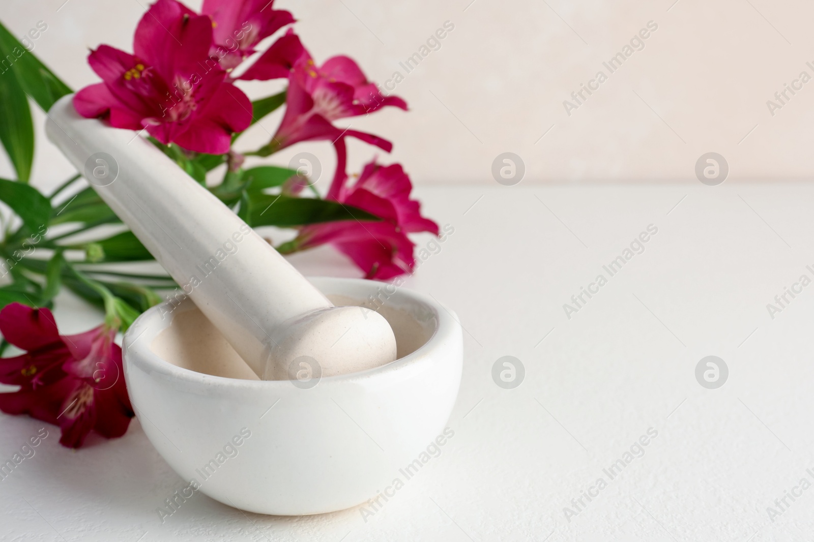 Ceramic mortar, pestle and flowers on white table, closeup. Space for text Photo of Ceramic mortar, pestle and flowers on white table, closeup. Space for text