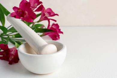 Photo of Ceramic mortar, pestle and flowers on white table, closeup. Space for text