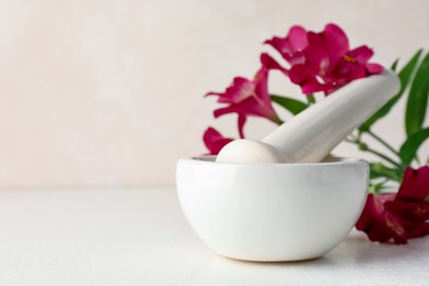 Photo of Ceramic mortar, pestle and flowers on white table, closeup. Space for text