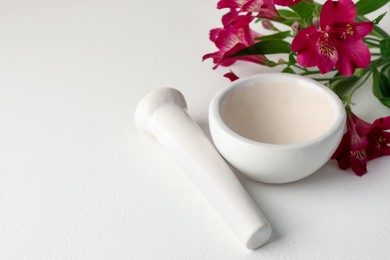 Photo of Ceramic mortar, pestle and flowers on white table, closeup. Space for text