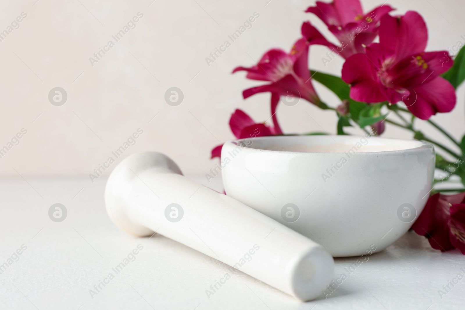 Ceramic mortar, pestle and flowers on white table, closeup Photo of Ceramic mortar, pestle and flowers on white table, closeup