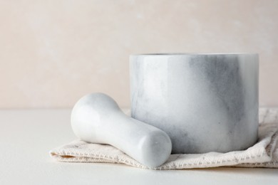 Photo of Marble mortar, pestle and cloth on white table, closeup
