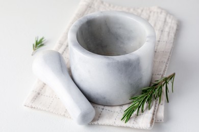 Photo of Marble mortar with rosemary, pestle and cloth on white table, closeup