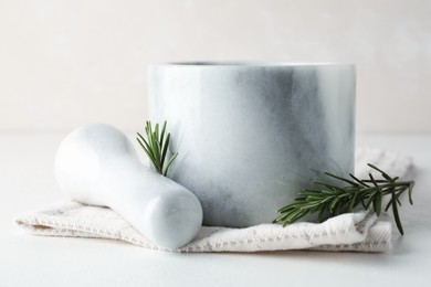 Photo of Marble mortar with rosemary, pestle and cloth on white table, closeup