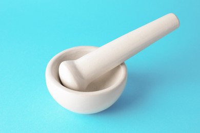 Photo of Ceramic mortar and pestle on light blue background, closeup