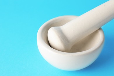 Photo of Ceramic mortar and pestle on light blue background, closeup