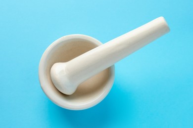 Photo of Ceramic mortar and pestle on light blue background, top view