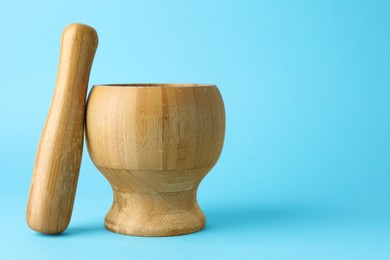 Photo of Wooden mortar and pestle on light blue background, closeup. Space for text