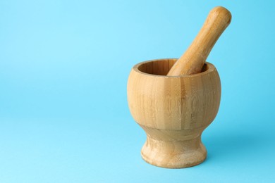 Photo of Wooden mortar and pestle on light blue background, closeup. Space for text