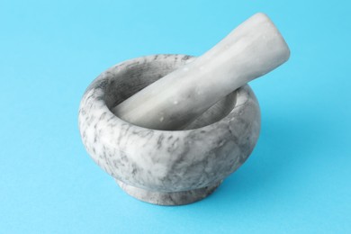 Photo of Marble mortar and pestle on light blue background, closeup