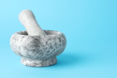 Photo of Marble mortar and pestle on light blue background, closeup. Space for text