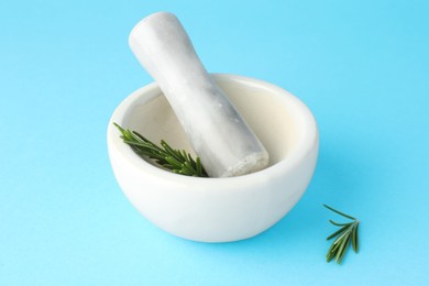 Photo of Ceramic mortar with rosemary and pestle on light blue background, closeup