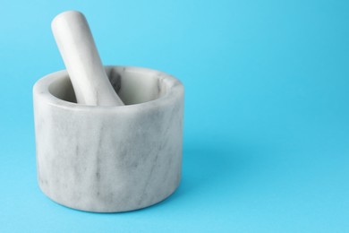 Photo of Marble mortar and pestle on light blue background, closeup. Space for text