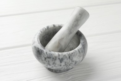 Photo of Marble mortar and pestle on white wooden table, closeup