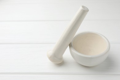 Photo of Ceramic mortar and pestle on white wooden table. Space for text