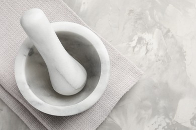 Photo of Marble mortar, pestle and cloth on grey textured table, top view. Space for text