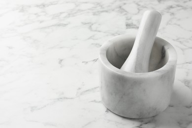 Photo of Mortar and pestle on white marble table, closeup. Space for text