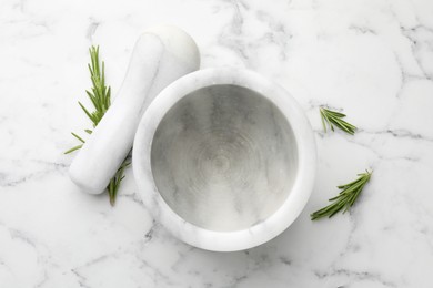 Photo of Mortar with rosemary and pestle on white marble table, flat lay