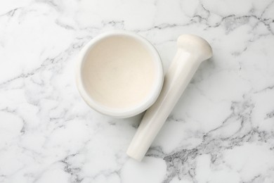 Photo of Ceramic mortar and pestle on white marble table, top view