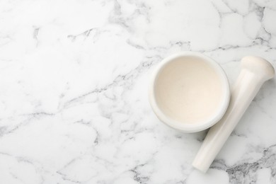 Photo of Ceramic mortar and pestle on white marble table, top view. Space for text