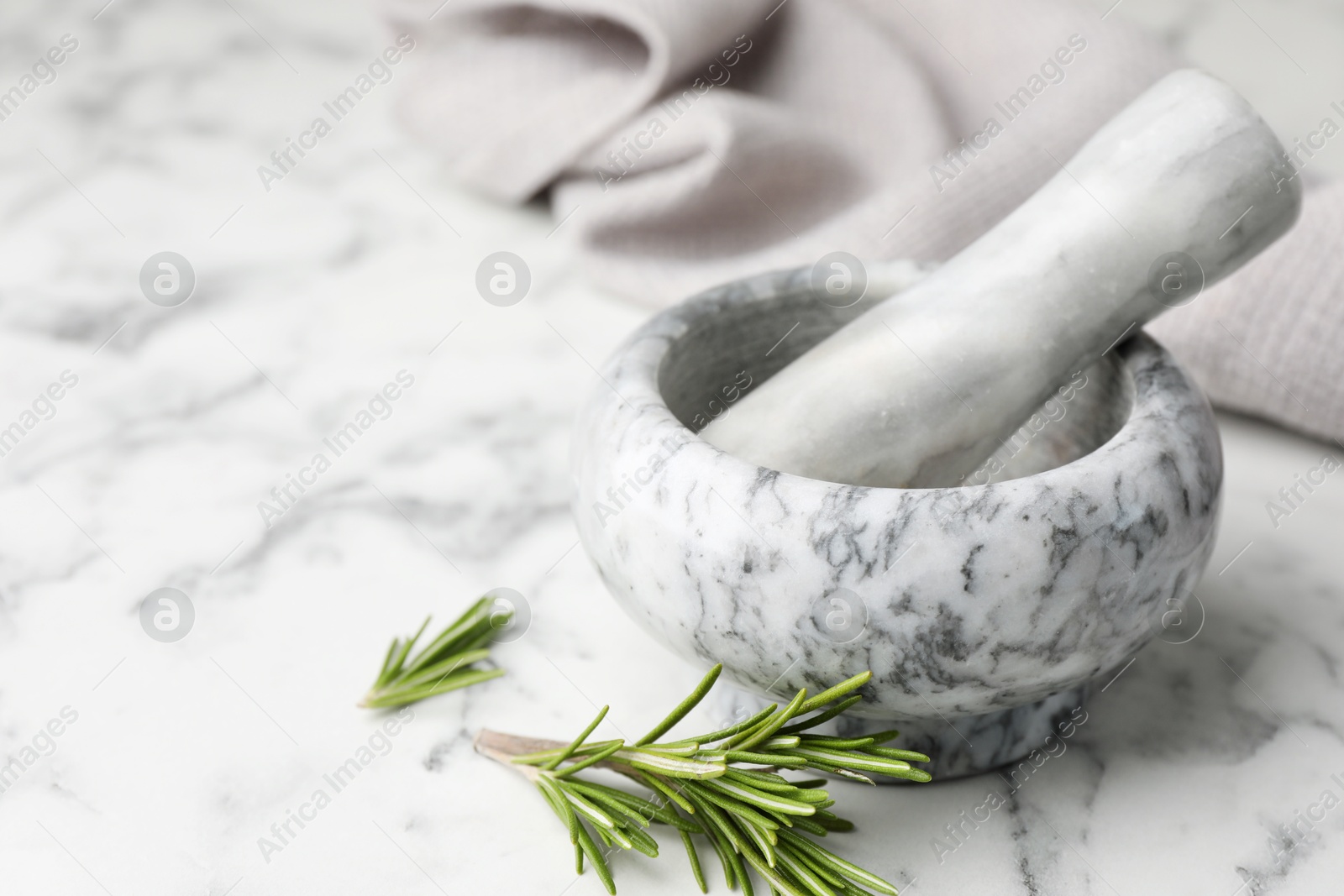 Mortar with rosemary, pestle and cloth on white marble table, closeup. Space for text Photo of Mortar with rosemary, pestle and cloth on white marble table, closeup. Space for text