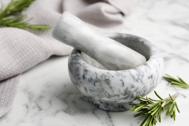 Photo of Mortar with rosemary, pestle and cloth on white marble table, closeup