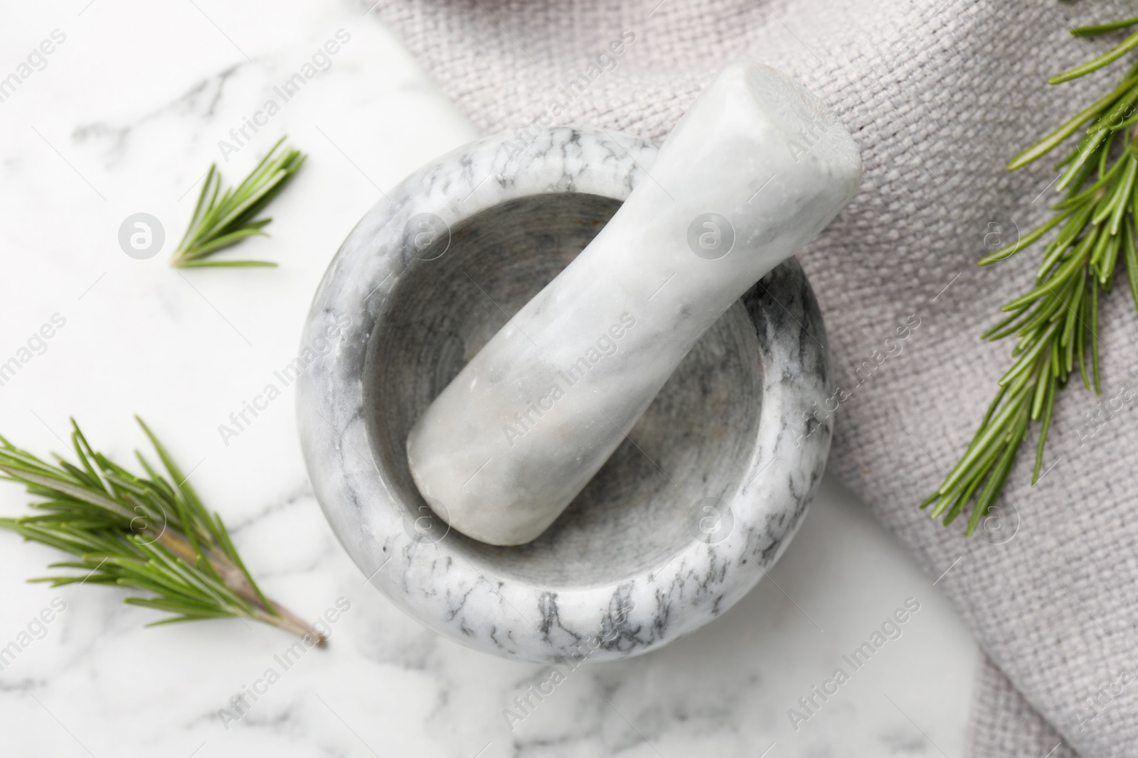 Mortar with rosemary, pestle and cloth on white marble table, flat lay Photo of Mortar with rosemary, pestle and cloth on white marble table, flat lay