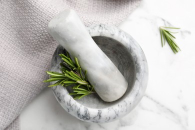 Photo of Mortar with rosemary, pestle and cloth on white marble table, flat lay