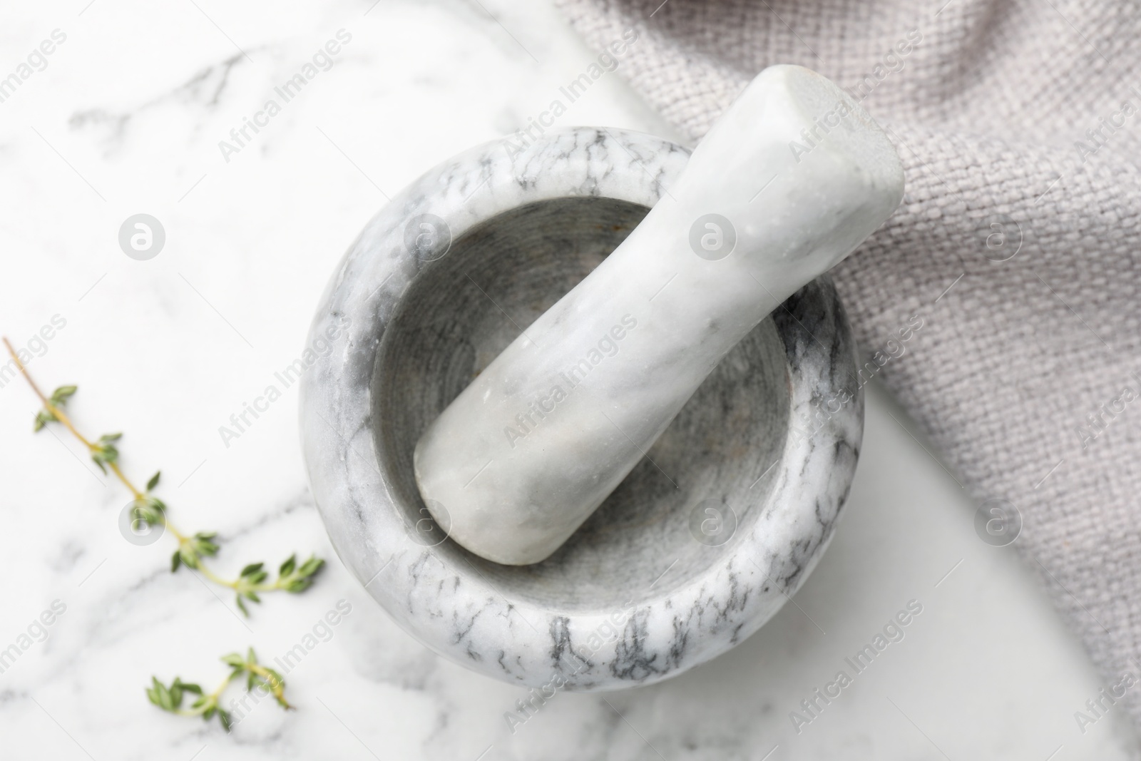 Mortar with thyme, pestle and cloth on white marble table, flat lay Photo of Mortar with thyme, pestle and cloth on white marble table, flat lay
