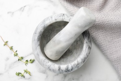 Photo of Mortar with thyme, pestle and cloth on white marble table, flat lay