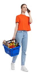 Photo of Woman with shopping basket full of products talking on phone against white background