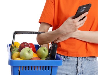 Photo of Woman with shopping basket full of products and smartphone on white background, closeup