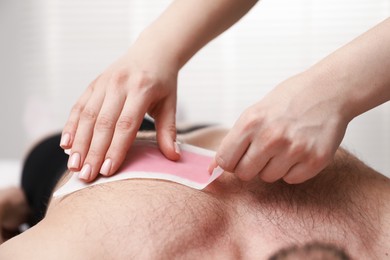 Photo of Young man undergoing wax epilation in salon, closeup