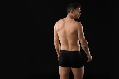 Photo of Young man in stylish underwear on black background, back view. Space for text