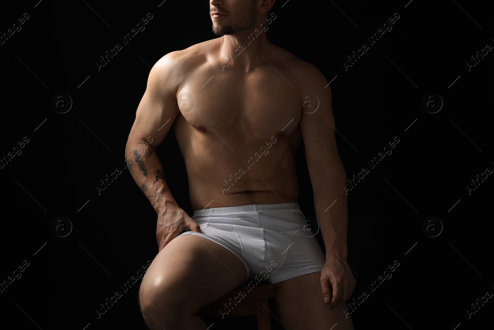 Young man in stylish white underwear on chair against black background, closeup Photo of Young man in stylish white underwear on chair against black background, closeup