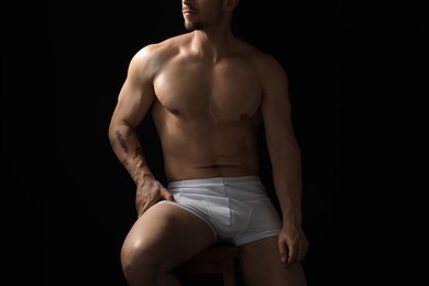 Photo of Young man in stylish white underwear on chair against black background, closeup
