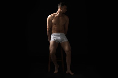 Photo of Young man in stylish white underwear on chair against black background