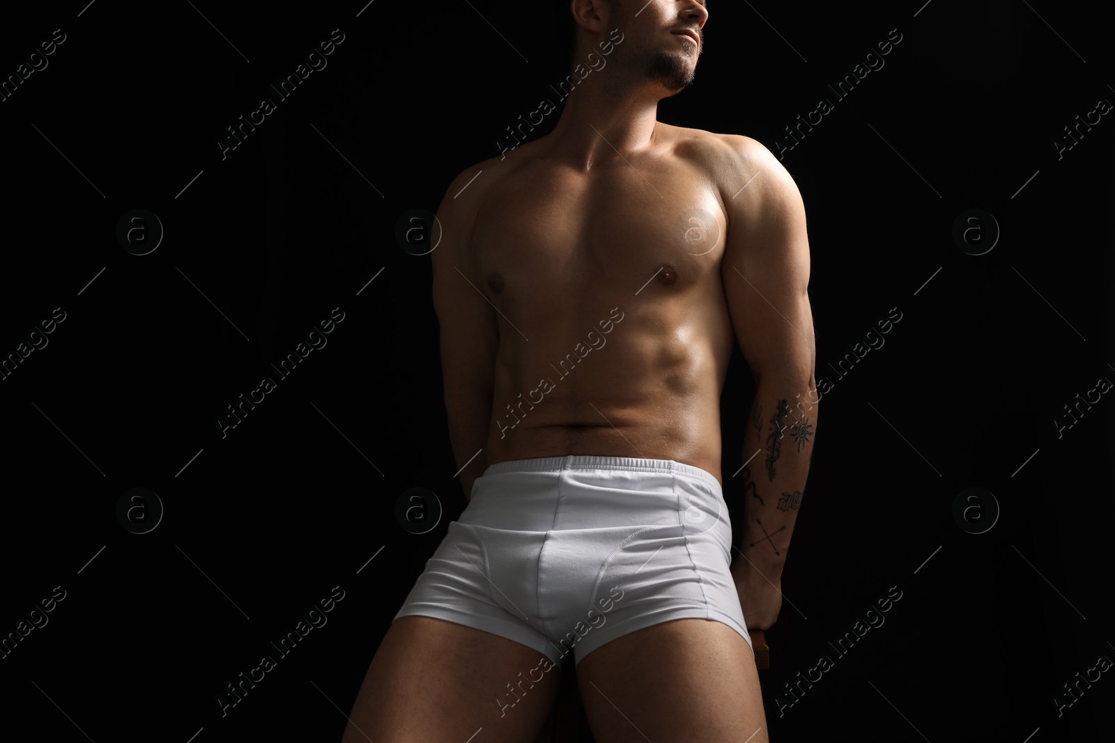 Young man in stylish white underwear on chair against black background, closeup Photo of Young man in stylish white underwear on chair against black background, closeup