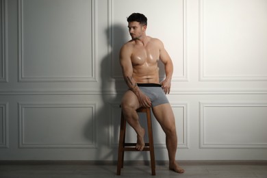 Photo of Young man in stylish light grey underwear on chair near white wall indoors