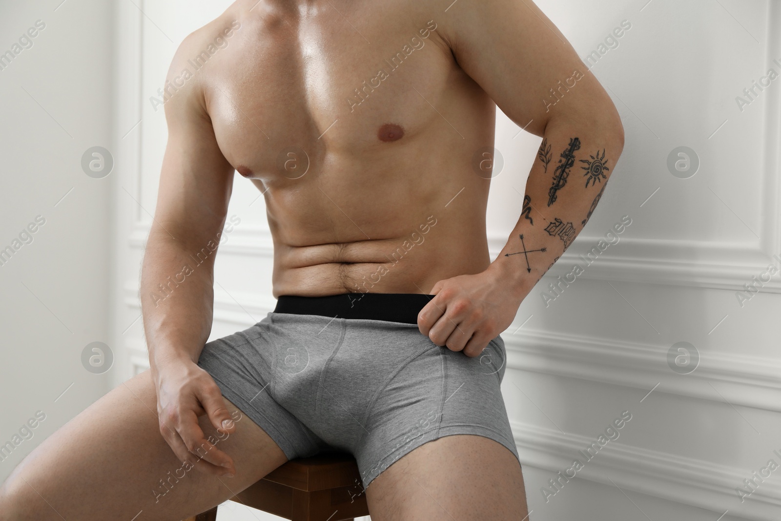 Young man in stylish light grey underwear on chair near white wall indoors, closeup Photo of Young man in stylish light grey underwear on chair near white wall indoors, closeup