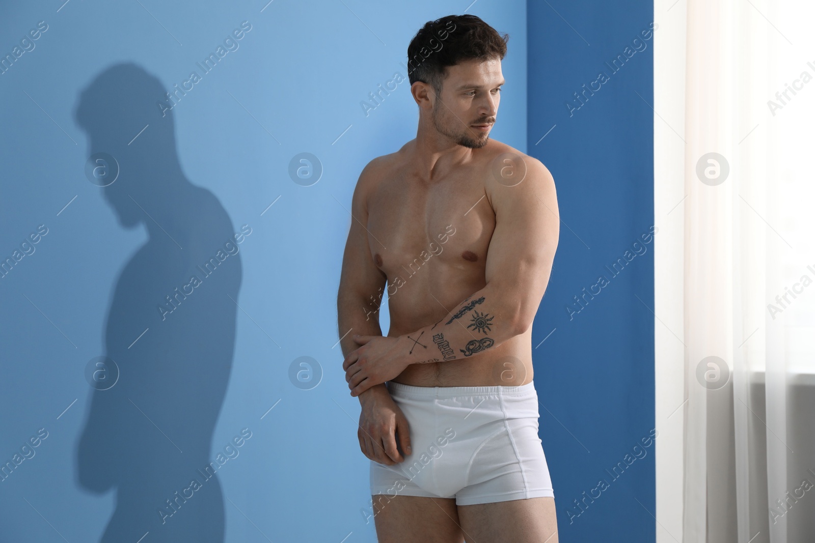 Young man in stylish white underwear near light blue wall indoors Photo of Young man in stylish white underwear near light blue wall indoors