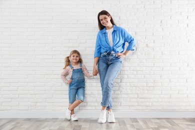 Photo of Beautiful mother and her little daughter near white brick wall