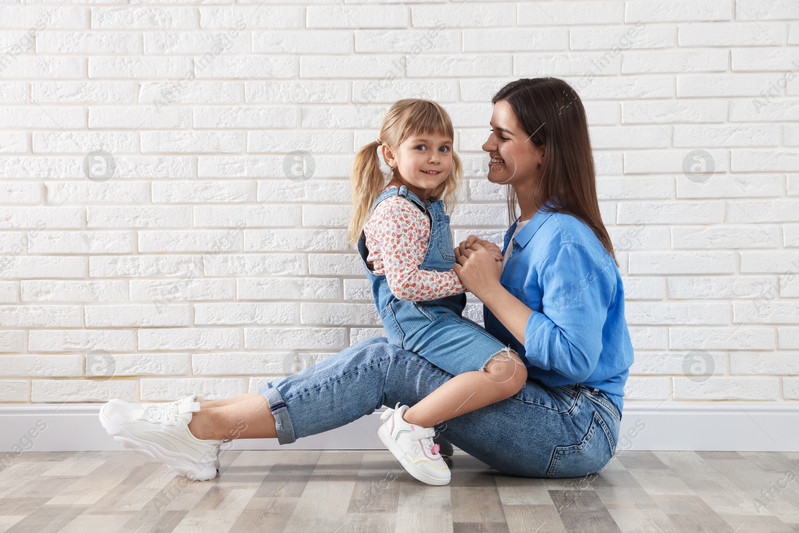 Beautiful mother and her little daughter near white brick wall. Space for text Photo of Beautiful mother and her little daughter near white brick wall. Space for text