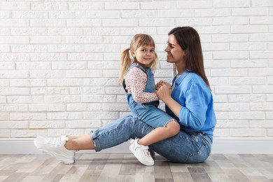 Photo of Beautiful mother and her little daughter near white brick wall. Space for text