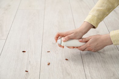 Photo of Young woman spraying insecticide onto cockroaches on floor at home, closeup. Pest problem