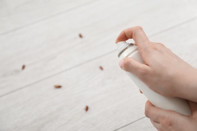 Photo of Young woman spraying insecticide onto cockroaches on floor at home, closeup. Pest problem
