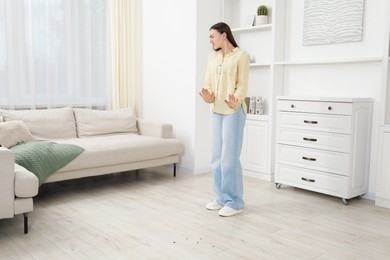 Photo of Emotional young woman looking in disgust at cockroaches on floor indoors. Pest problem