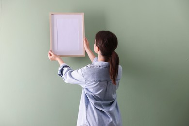 Photo of Woman hanging blank frame on green wall, back view