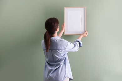 Photo of Woman hanging blank frame on green wall, back view